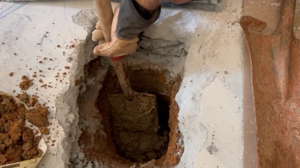 Worker digging soil through an opening cut in a concrete floor.