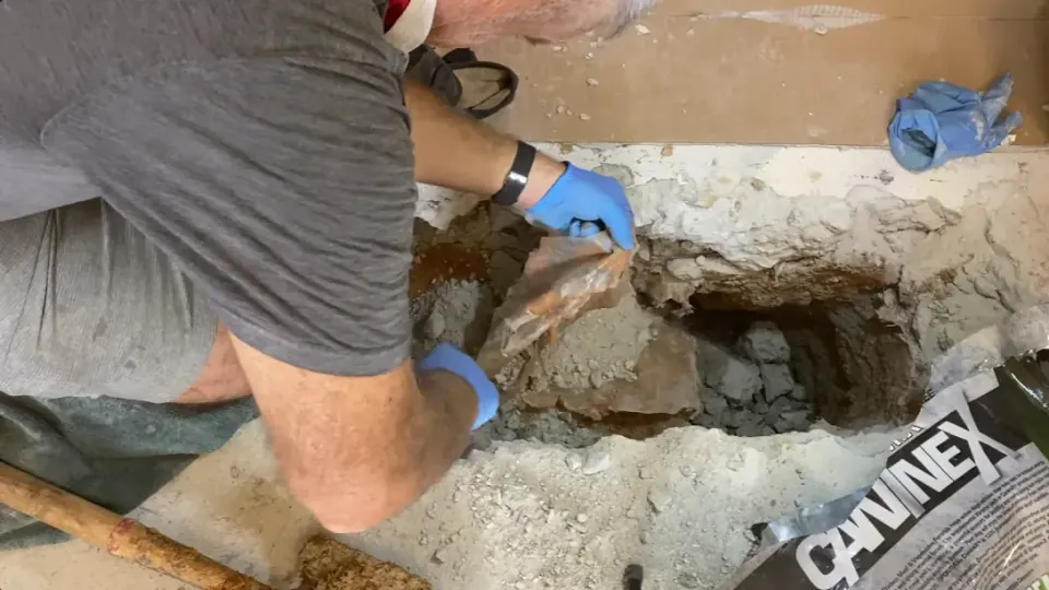 Worker removing broken material from an opening in a concrete floor.